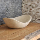 Switch Norhew luxury cream stone boat-shaped vessel sink with an organic sweeping rim and subtle natural veining on a wooden vanity. 3 image