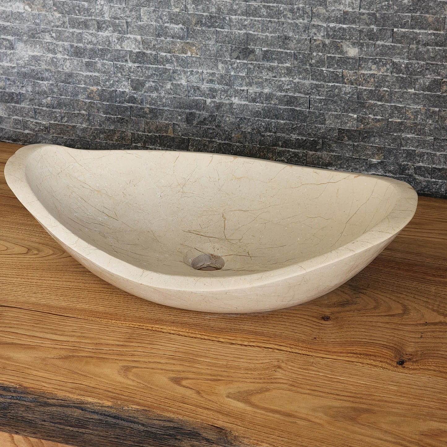 Norhew luxury cream stone boat-shaped vessel sink with an organic sweeping rim and subtle natural veining on a wooden vanity.