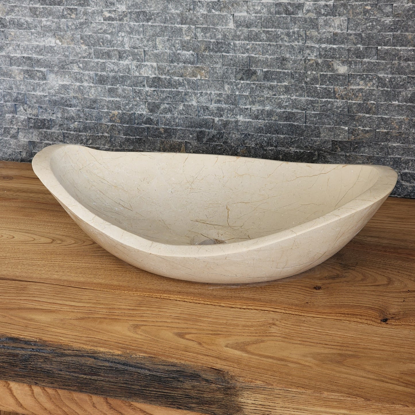 Norhew luxury cream stone boat-shaped vessel sink with an organic sweeping rim and subtle natural veining on a wooden vanity.