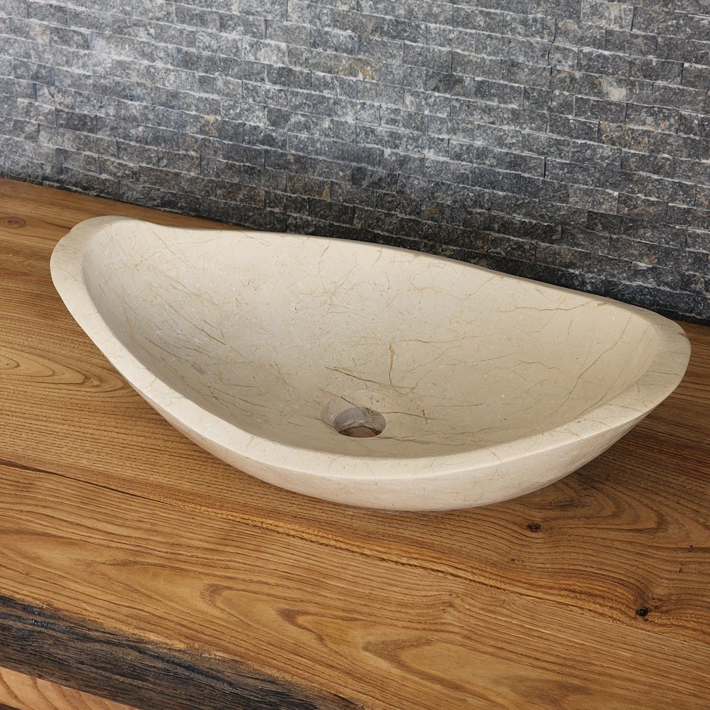 Norhew luxury cream stone boat-shaped vessel sink with an organic sweeping rim and subtle natural veining on a wooden vanity.