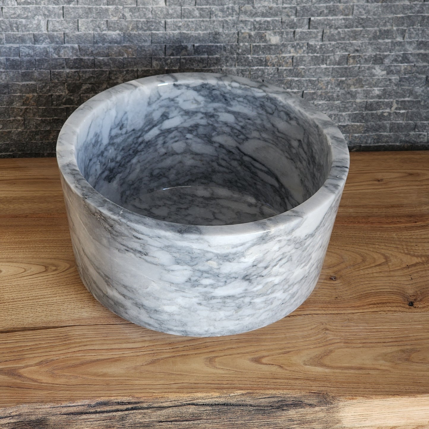 High-walled cylindrical marble vessel sink with grey veining on wood vanity.