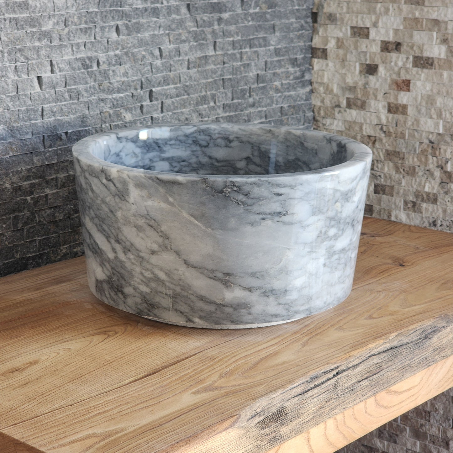 High-walled cylindrical marble vessel sink with grey veining on wood vanity.