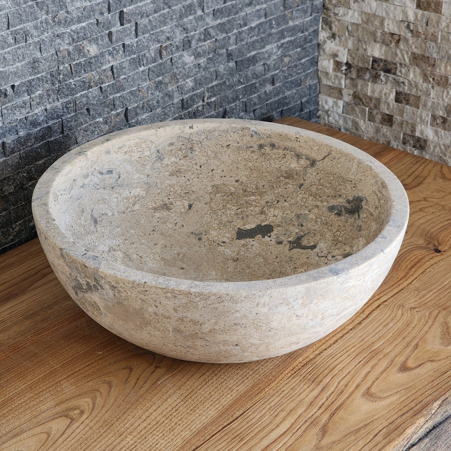 Norhew luxury round travertine vessel sink featuring an unrefined open-pore texture and a thick-walled bowl profile on a wooden vanity.