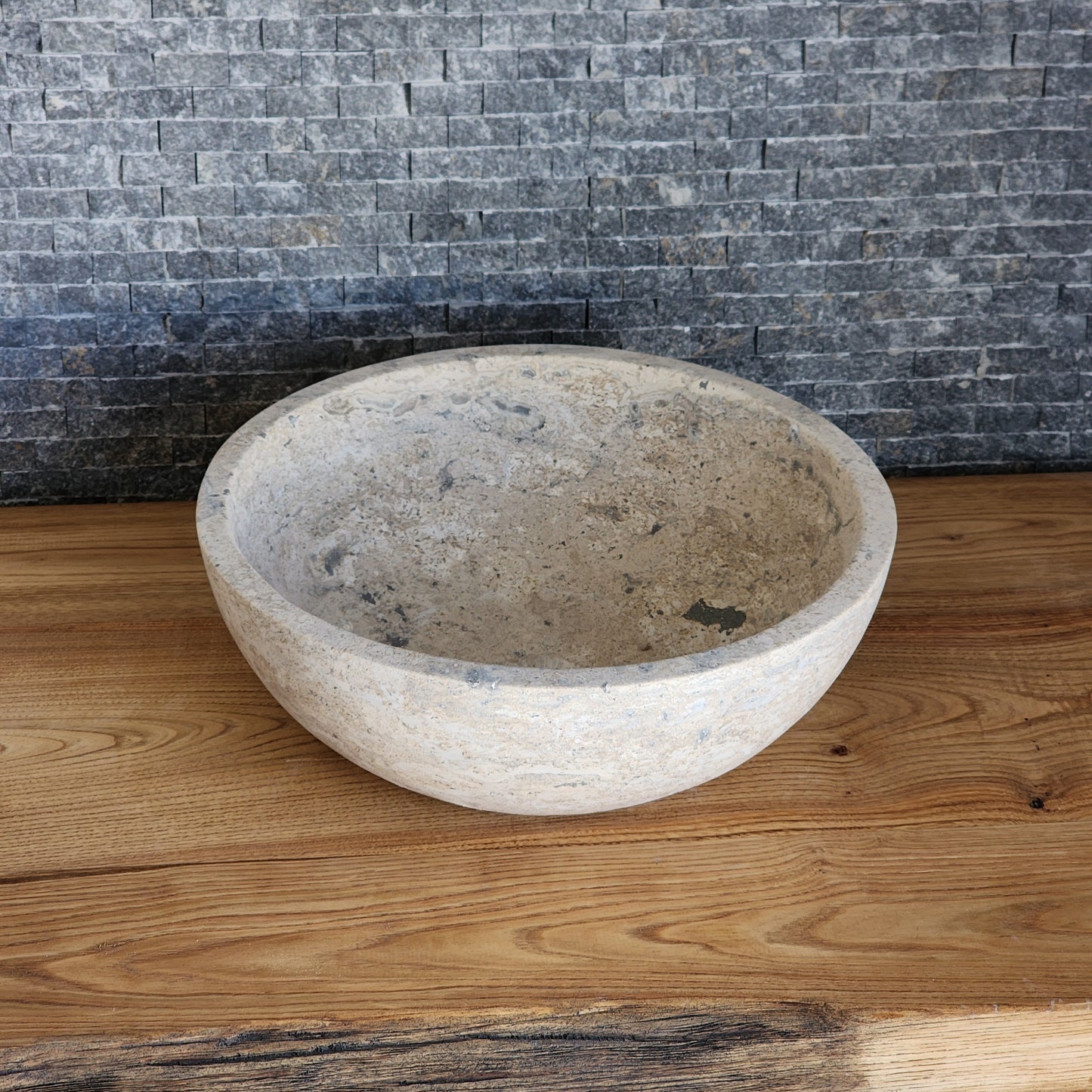 Norhew luxury round travertine vessel sink featuring an unrefined open-pore texture and a thick-walled bowl profile on a wooden vanity.