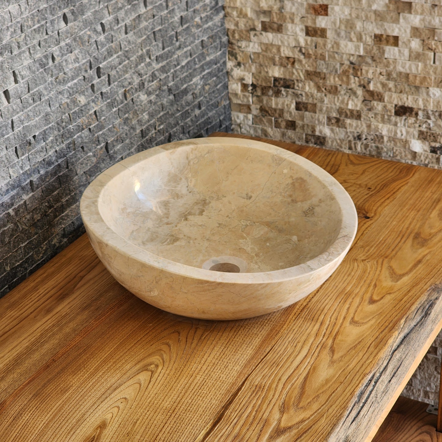 Hand-carved Norhew beige marble vessel sink featuring a polished finish and a unique asymmetrical slanted rim on a wood countertop.