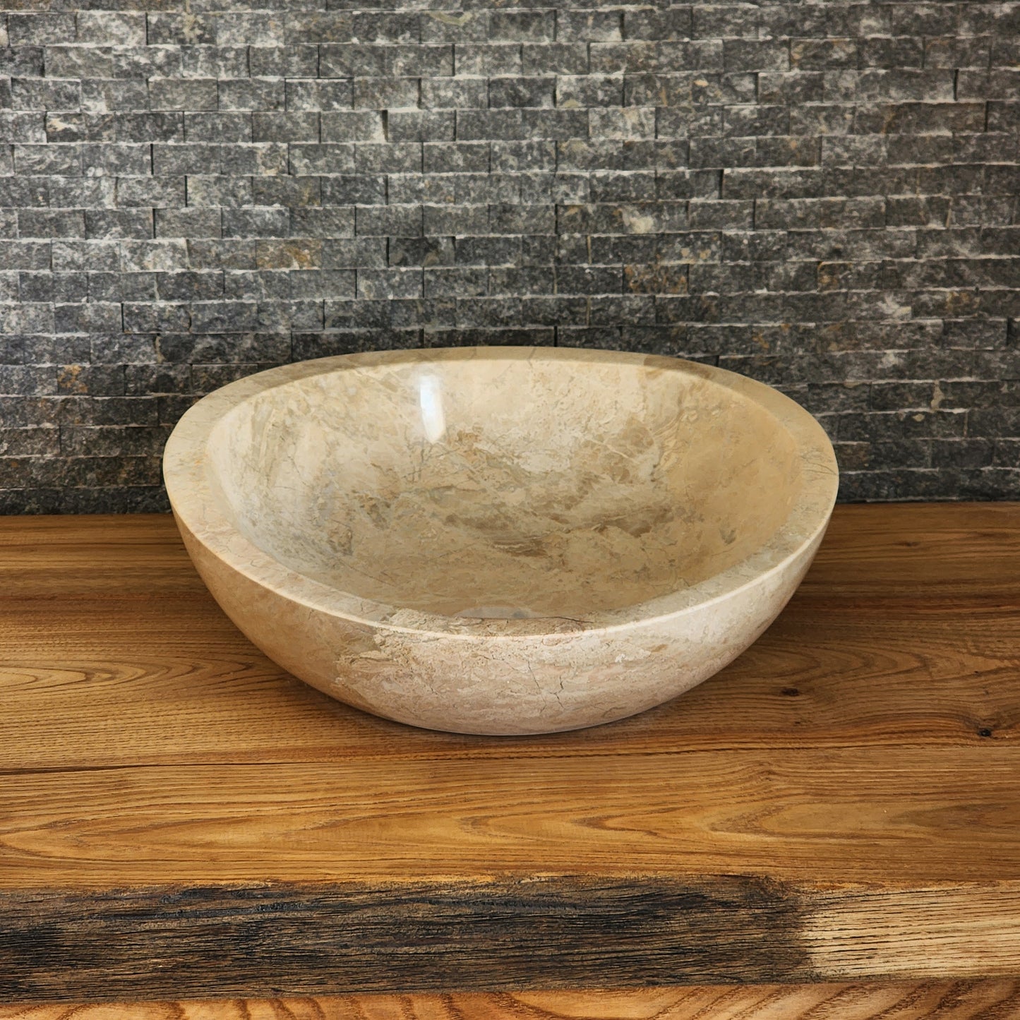 Hand-carved Norhew beige marble vessel sink featuring a polished finish and a unique asymmetrical slanted rim on a wood countertop.