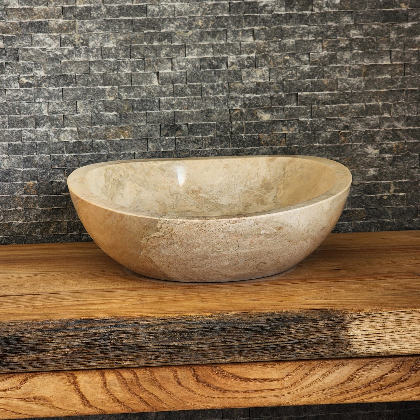Hand-carved Norhew beige marble vessel sink featuring a polished finish and a unique asymmetrical slanted rim on a wood countertop.