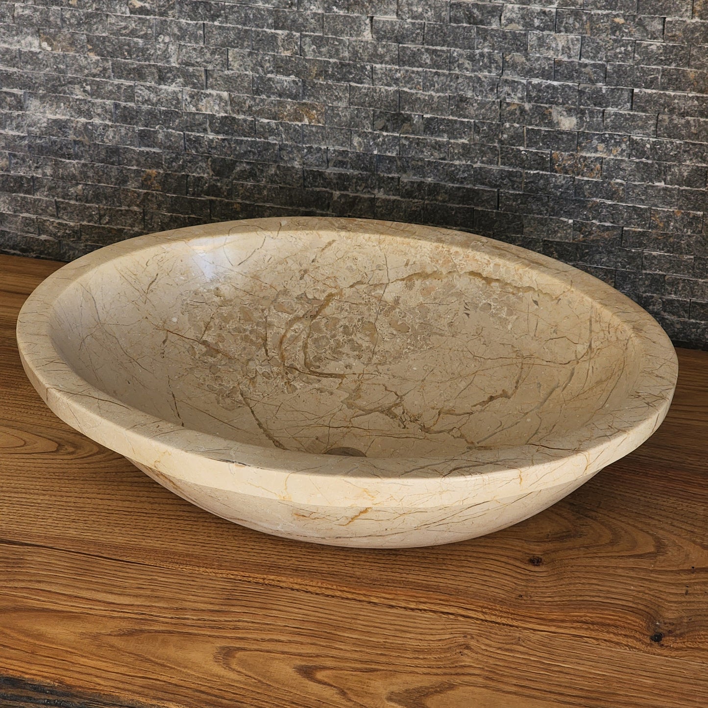 Norhew luxury oval beige breccia marble vessel sink with a classic flared rim and intricate natural veining on a wooden vanity.