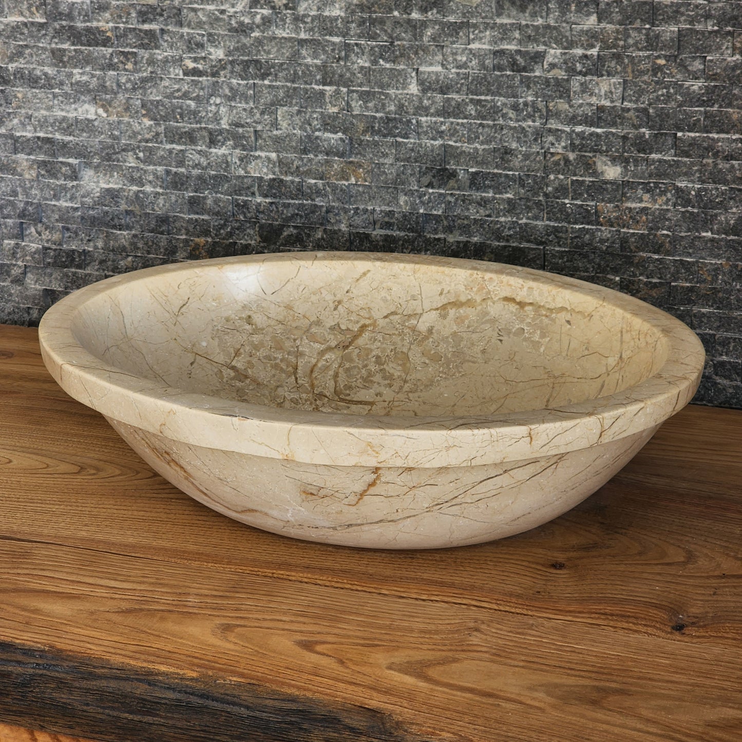 Norhew luxury oval beige breccia marble vessel sink with a classic flared rim and intricate natural veining on a wooden vanity.