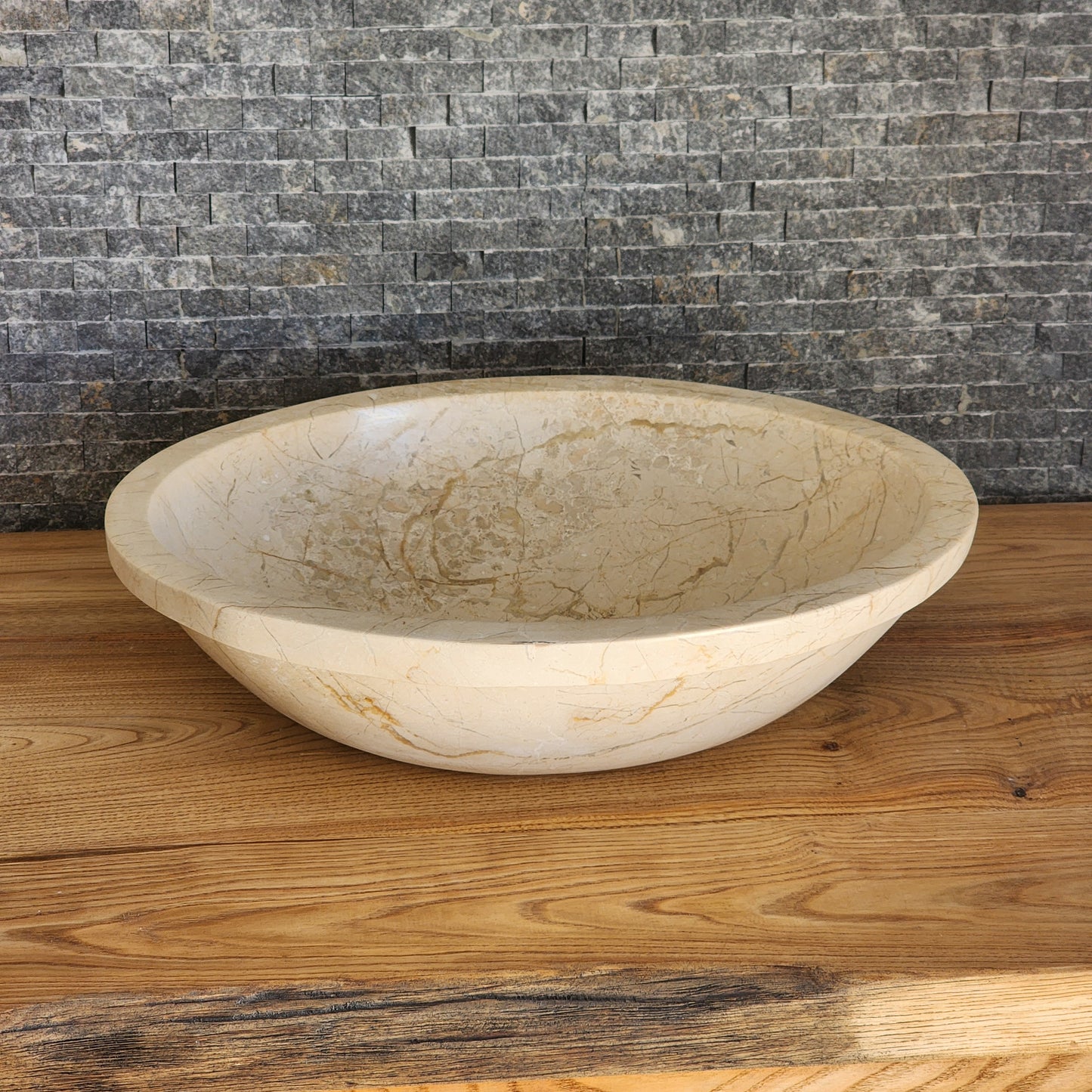 Norhew luxury oval beige breccia marble vessel sink with a classic flared rim and intricate natural veining on a wooden vanity.