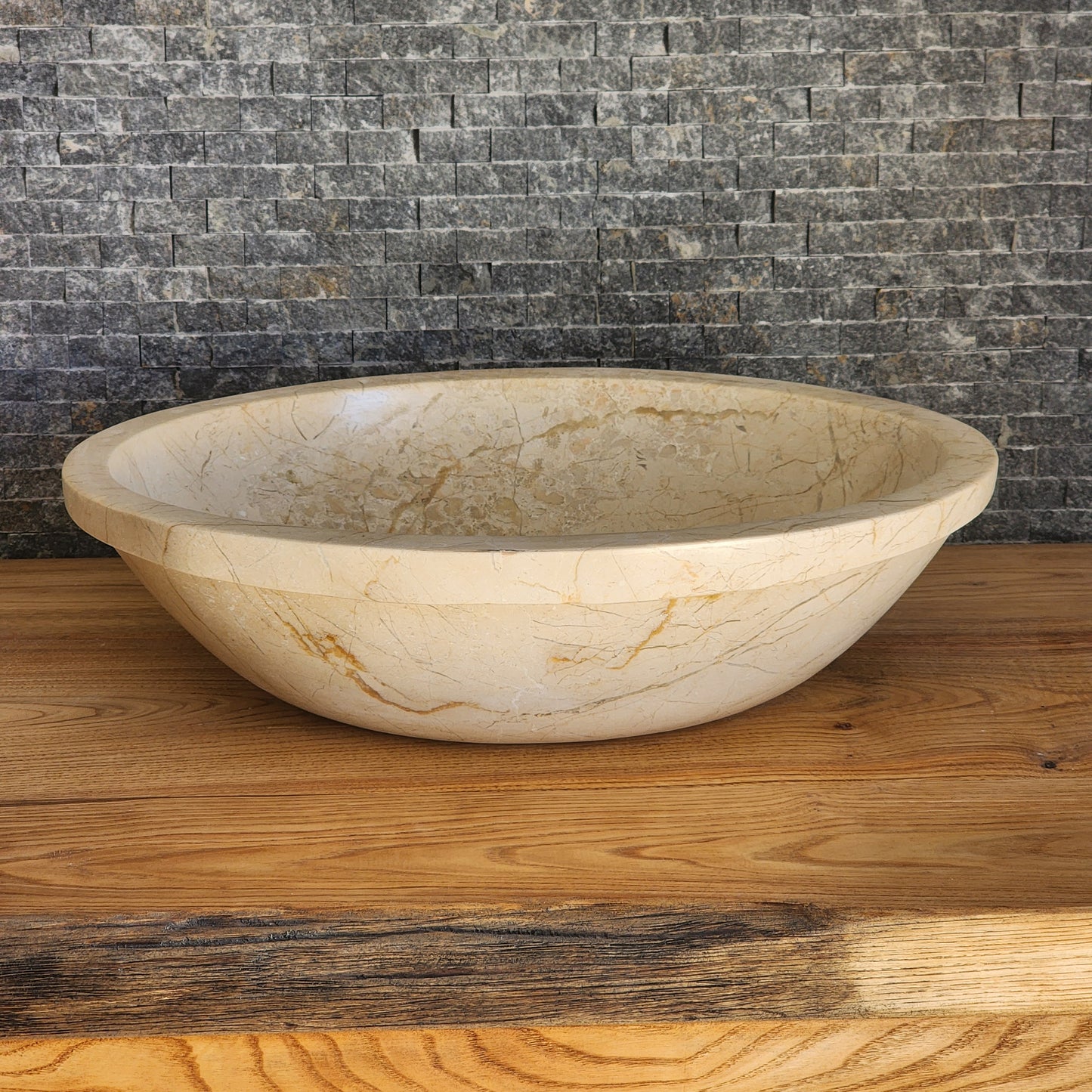 Norhew luxury oval beige breccia marble vessel sink with a classic flared rim and intricate natural veining on a wooden vanity.