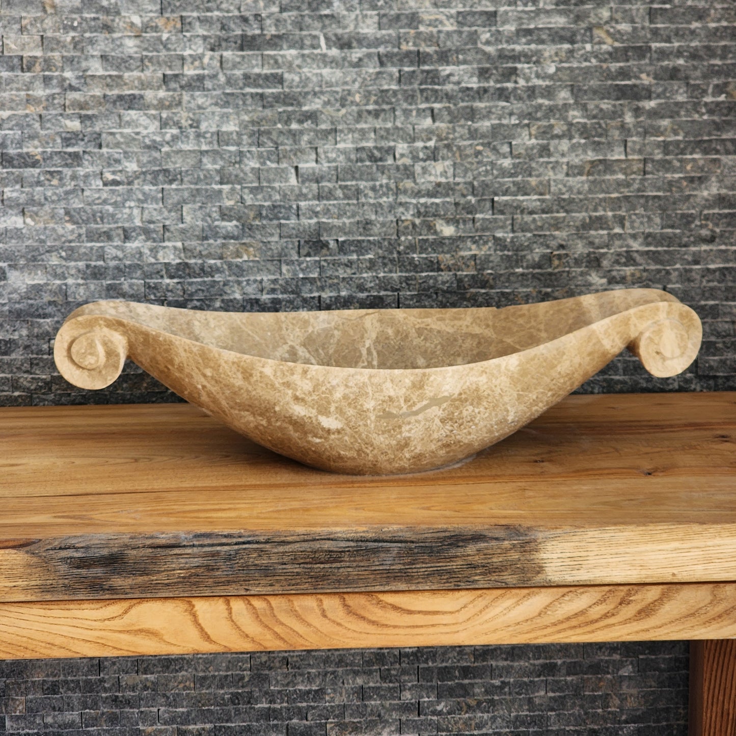 Norhew luxury beige marble boat-shaped vessel sink with hand-carved scroll spiral edges on a natural oak vanity.
