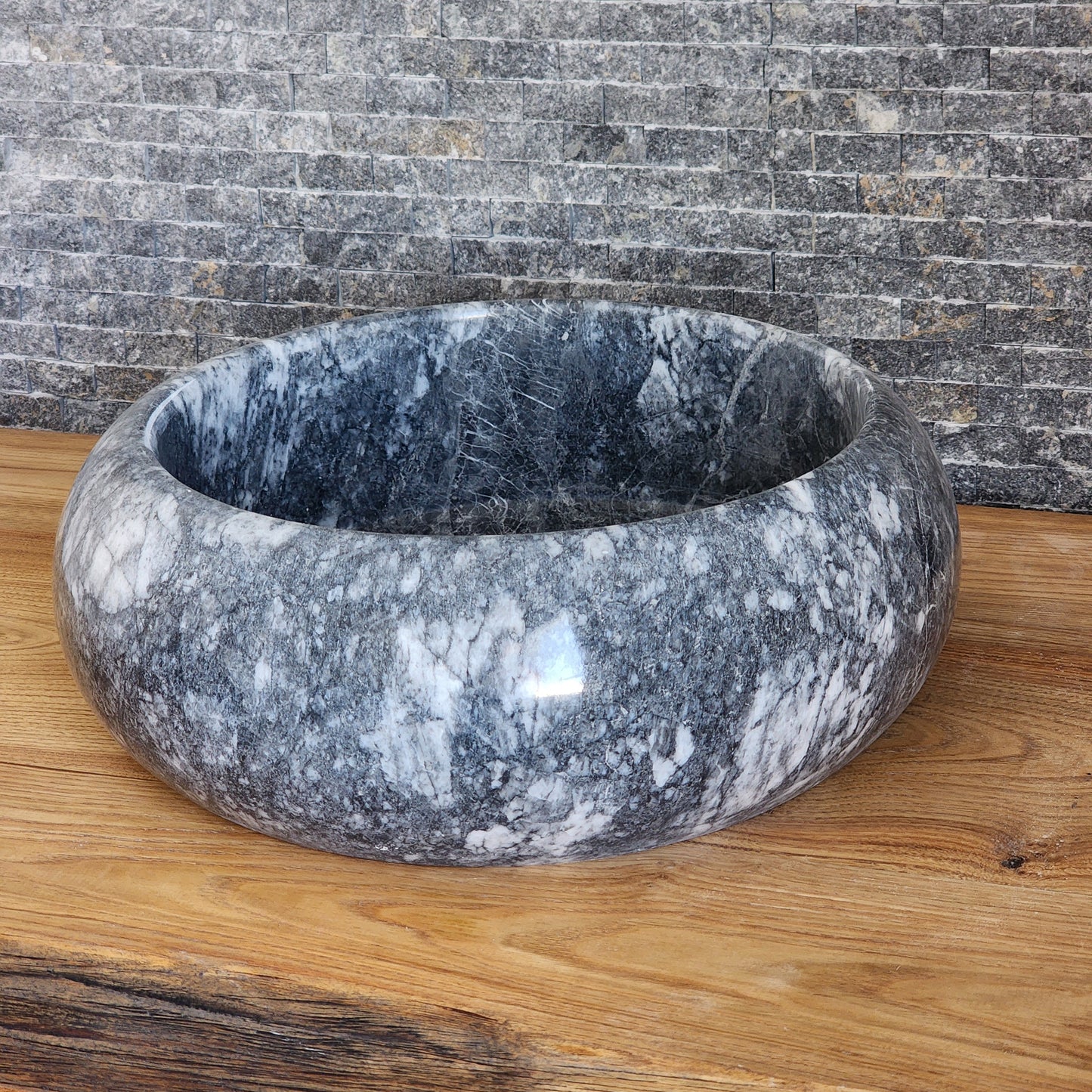 Norhew luxury round gray storm marble vessel sink with dramatic charcoal and white crystalline veining on a rustic oak vanity.