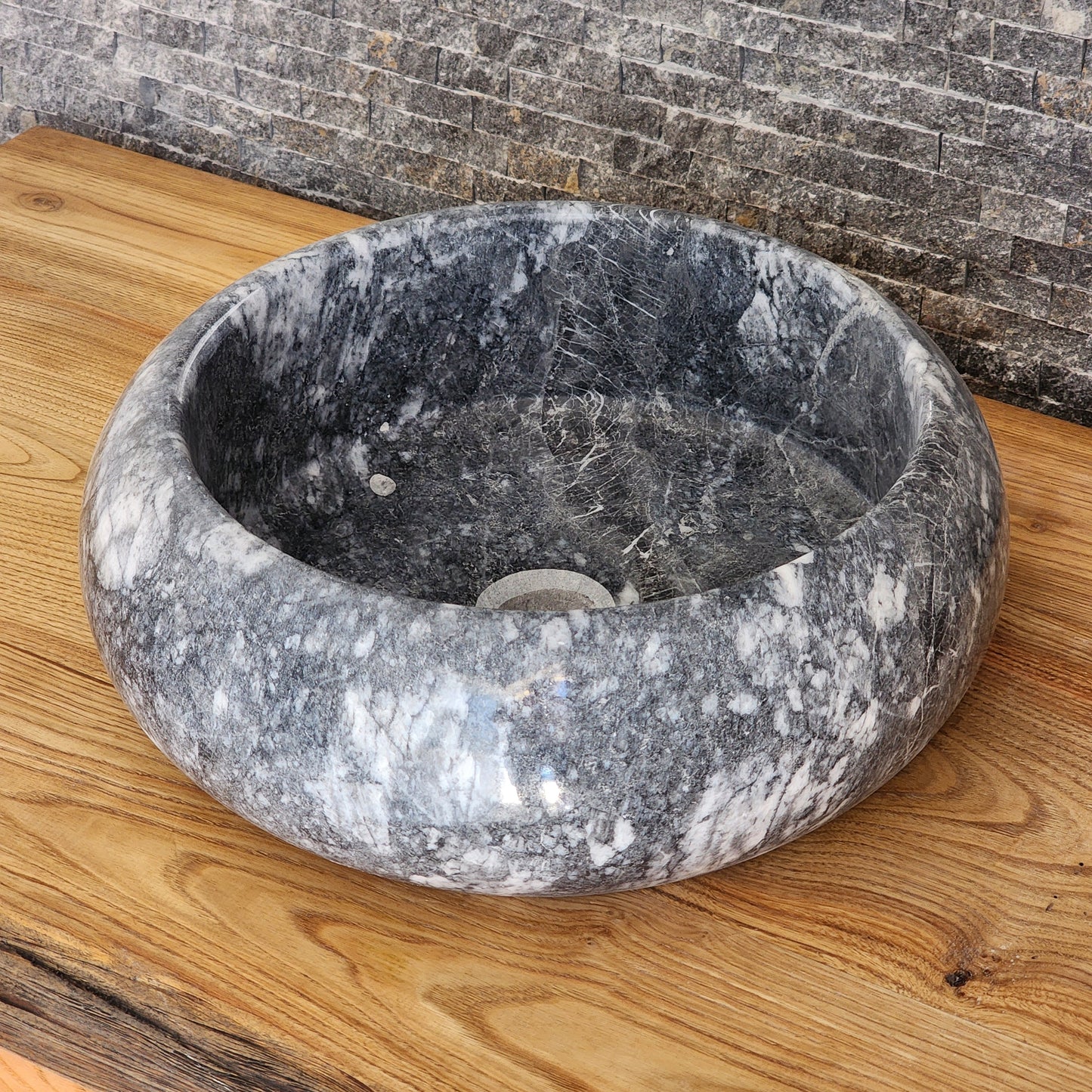 Norhew luxury round gray storm marble vessel sink with dramatic charcoal and white crystalline veining on a rustic oak vanity.