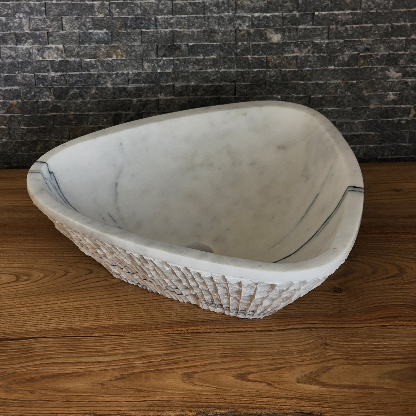 Norhew luxury triangular white marble vessel sink featuring a hand-chiseled raw exterior and a smooth interior with dramatic charcoal veining.