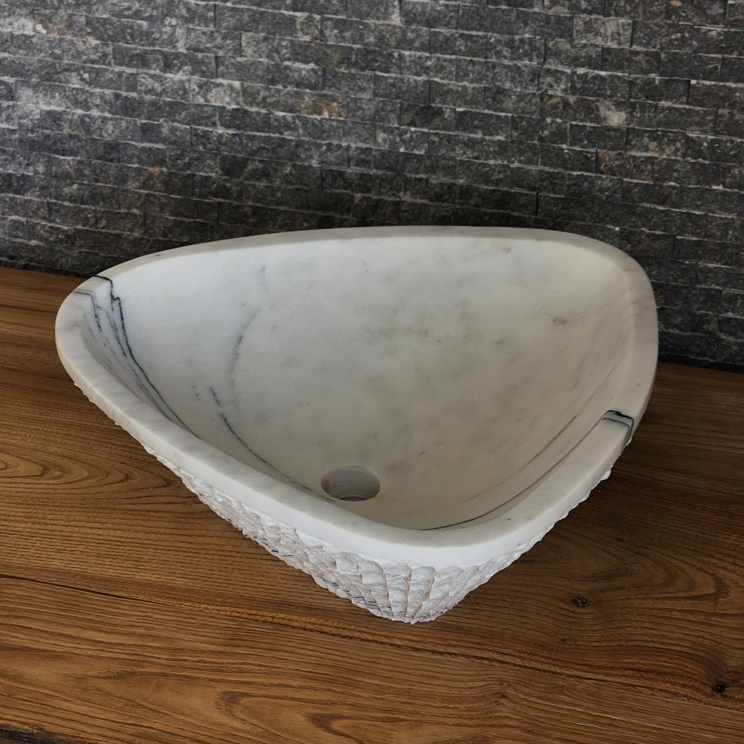 Norhew luxury triangular white marble vessel sink featuring a hand-chiseled raw exterior and a smooth interior with dramatic charcoal veining.