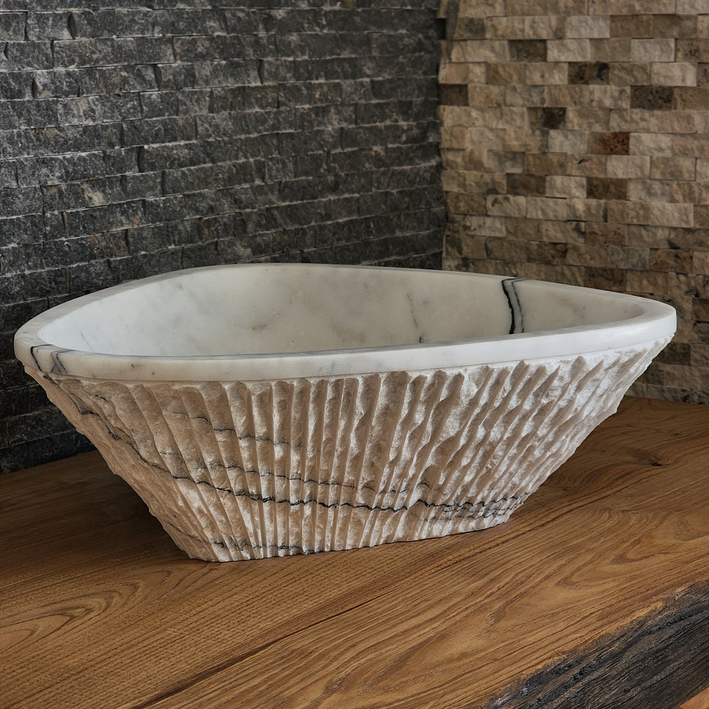 Norhew luxury triangular white marble vessel sink featuring a hand-chiseled raw exterior and a smooth interior with dramatic charcoal veining.