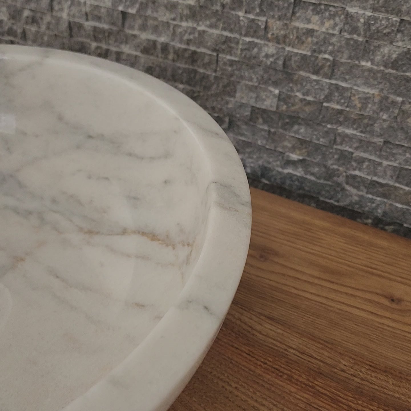 luxury round white marble vessel sink with a thick architectural rim and natural grey veining on a warm wood vanity.