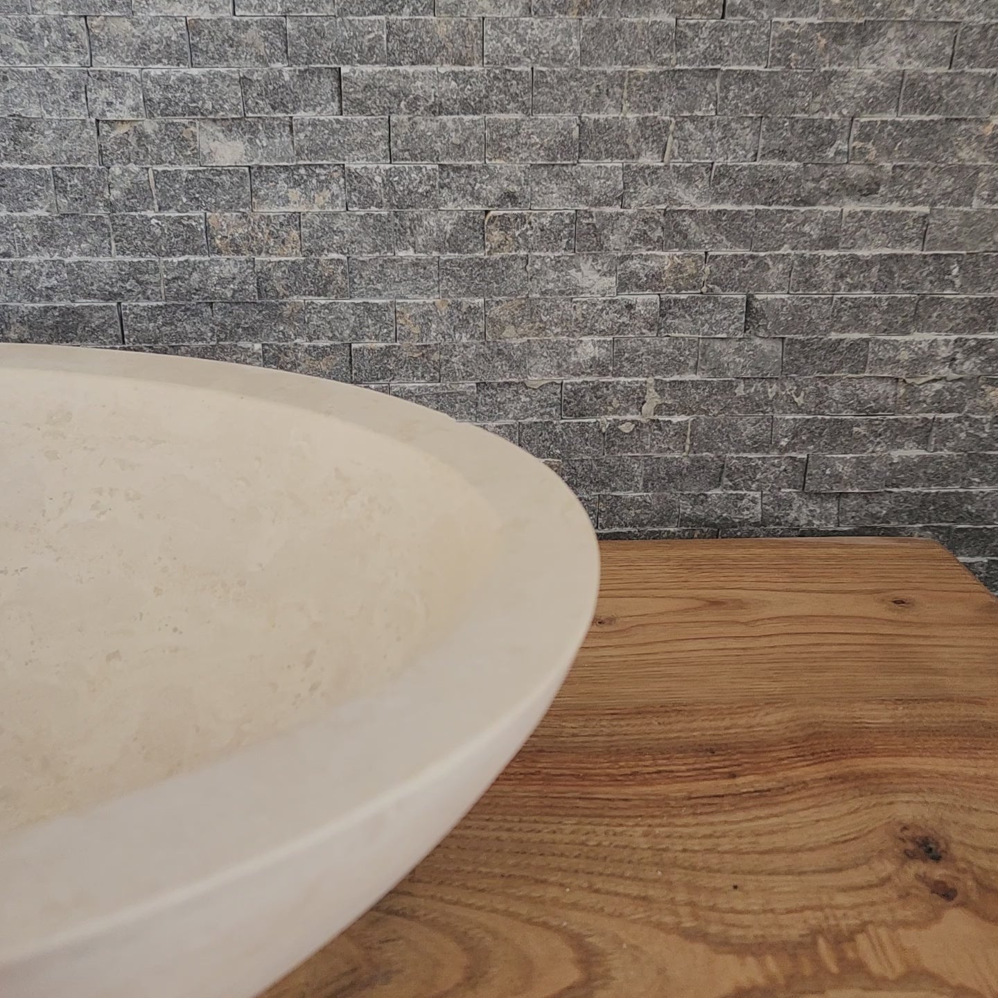 Norhew luxury round solid travertine vessel sink with natural golden-beige pitting and a thick-rimmed profile on a wooden vanity.