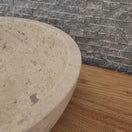 Switch Norhew luxury round travertine vessel sink featuring an unrefined open-pore texture and a thick-walled bowl profile on a wooden vanity. 2 image