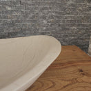 Switch Norhew luxury cream stone boat-shaped vessel sink with an organic sweeping rim and subtle natural veining on a wooden vanity. 2 image