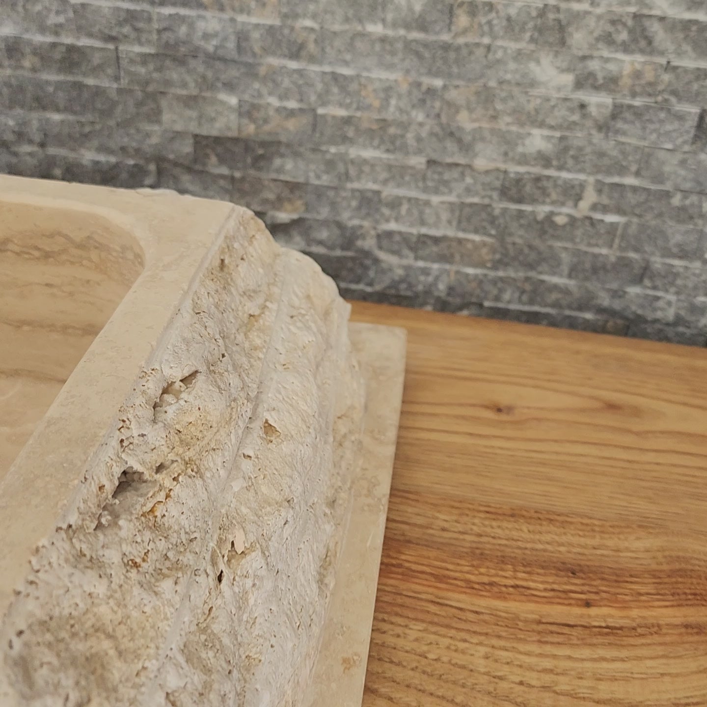 Norhew luxury rectangular travertine vessel sink featuring a chiseled raw stone exterior and a smooth honed interior on a wooden vanity.