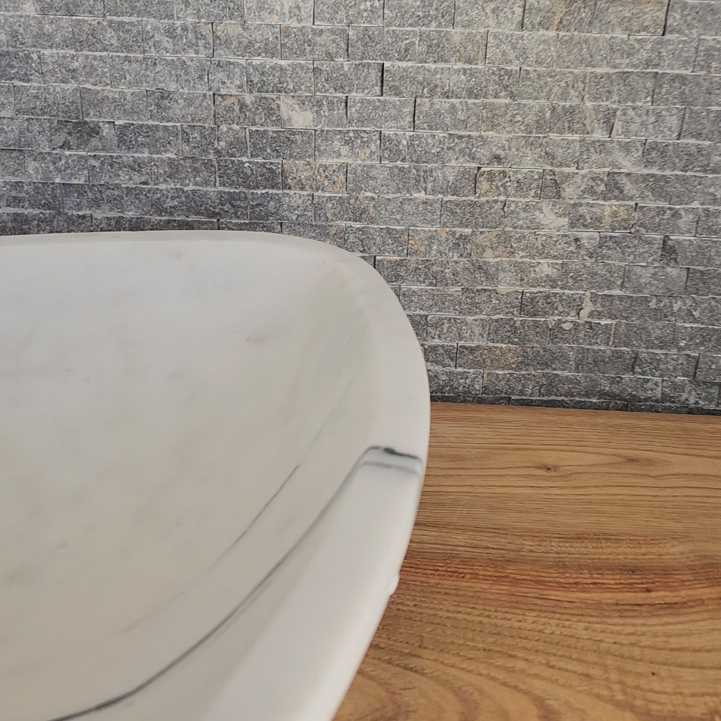 Norhew luxury triangular white marble vessel sink featuring a hand-chiseled raw exterior and a smooth interior with dramatic charcoal veining.