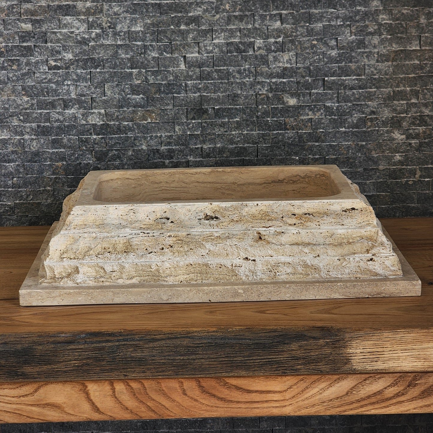 Norhew luxury rectangular travertine vessel sink featuring a chiseled raw stone exterior and a smooth honed interior on a wooden vanity.