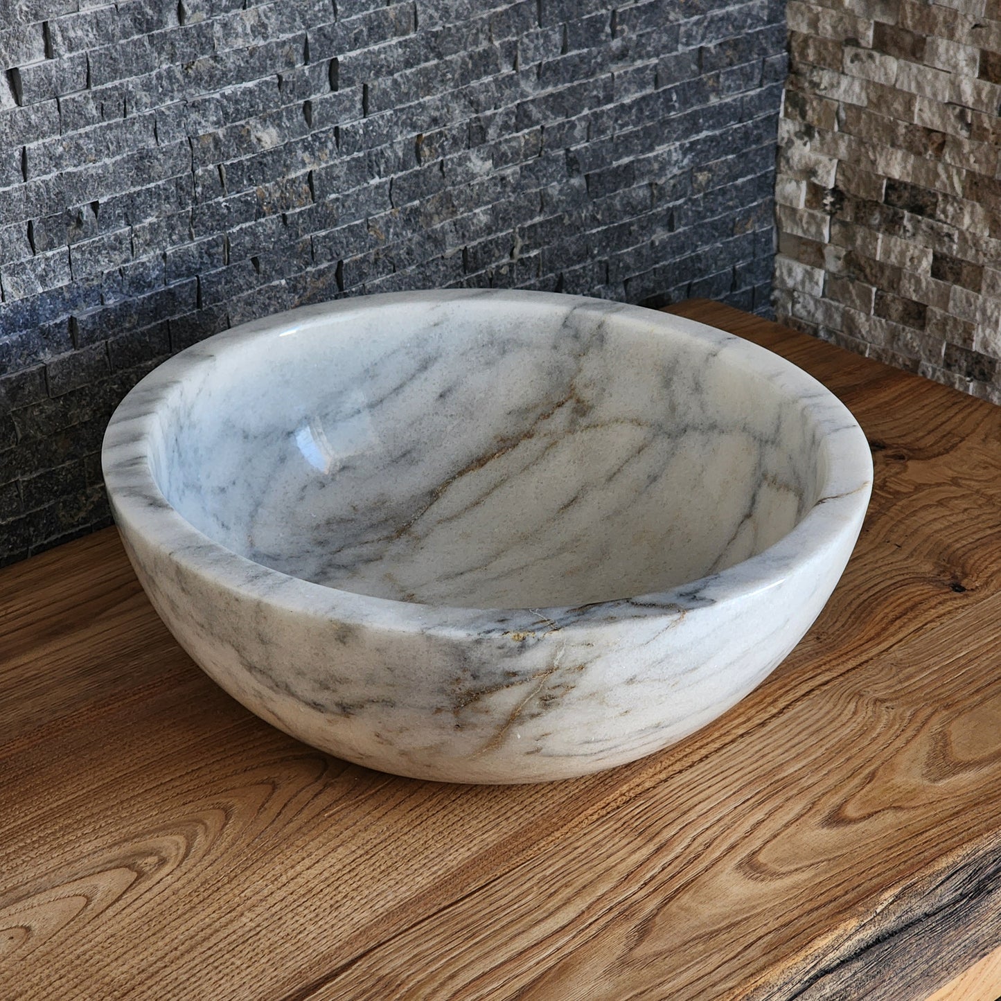 luxury round white marble vessel sink with a thick architectural rim and natural grey veining on a warm wood vanity.