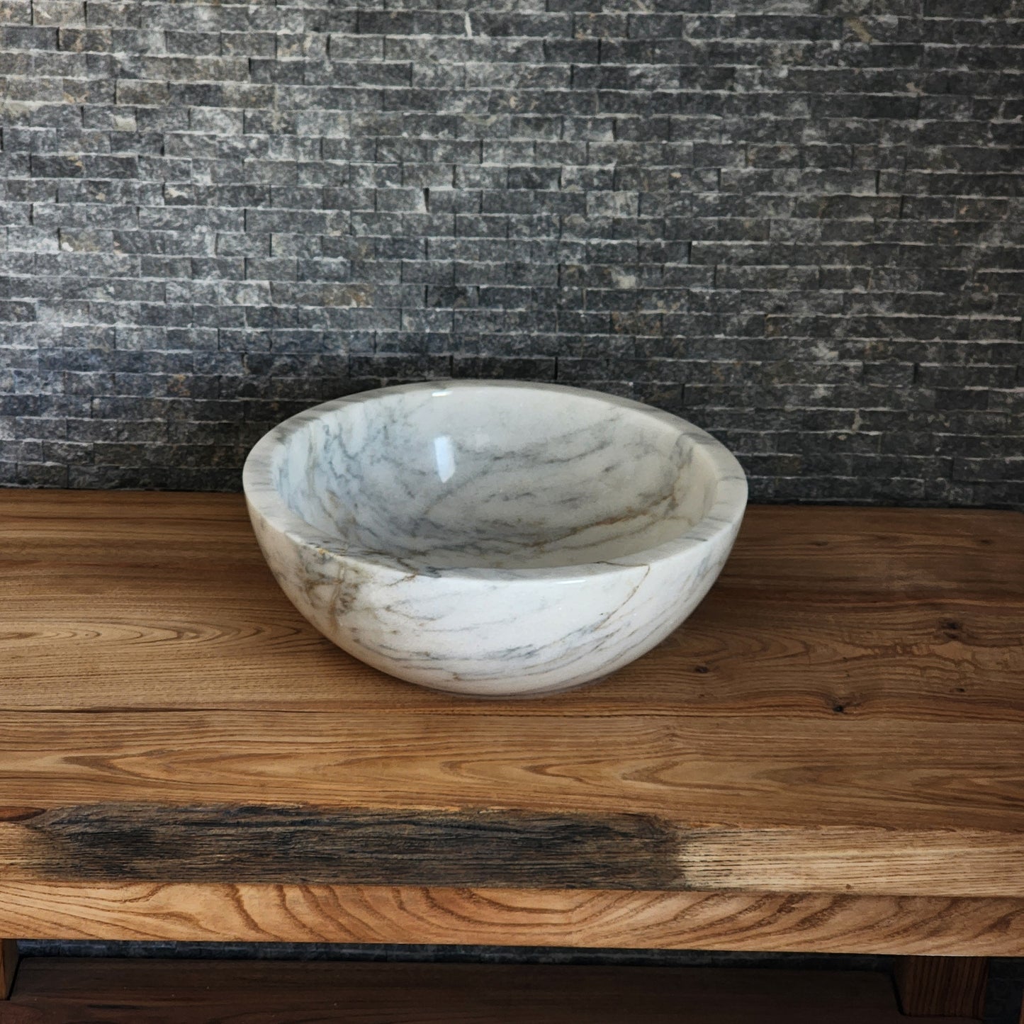 luxury round white marble vessel sink with a thick architectural rim and natural grey veining on a warm wood vanity.
