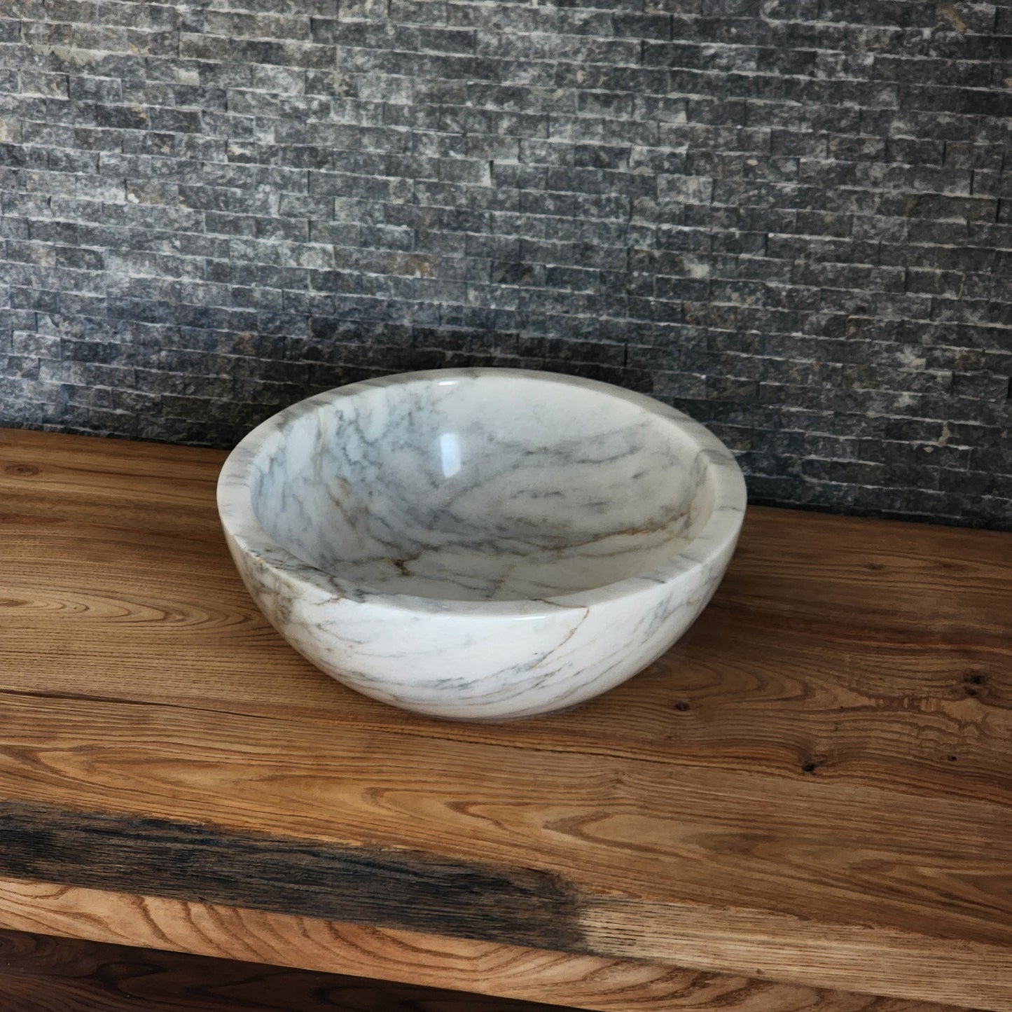 luxury round white marble vessel sink with a thick architectural rim and natural grey veining on a warm wood vanity.