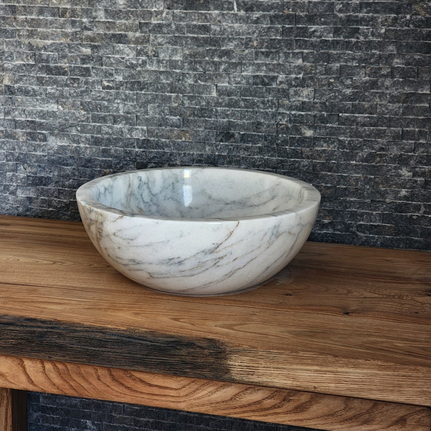 luxury round white marble vessel sink with a thick architectural rim and natural grey veining on a warm wood vanity.