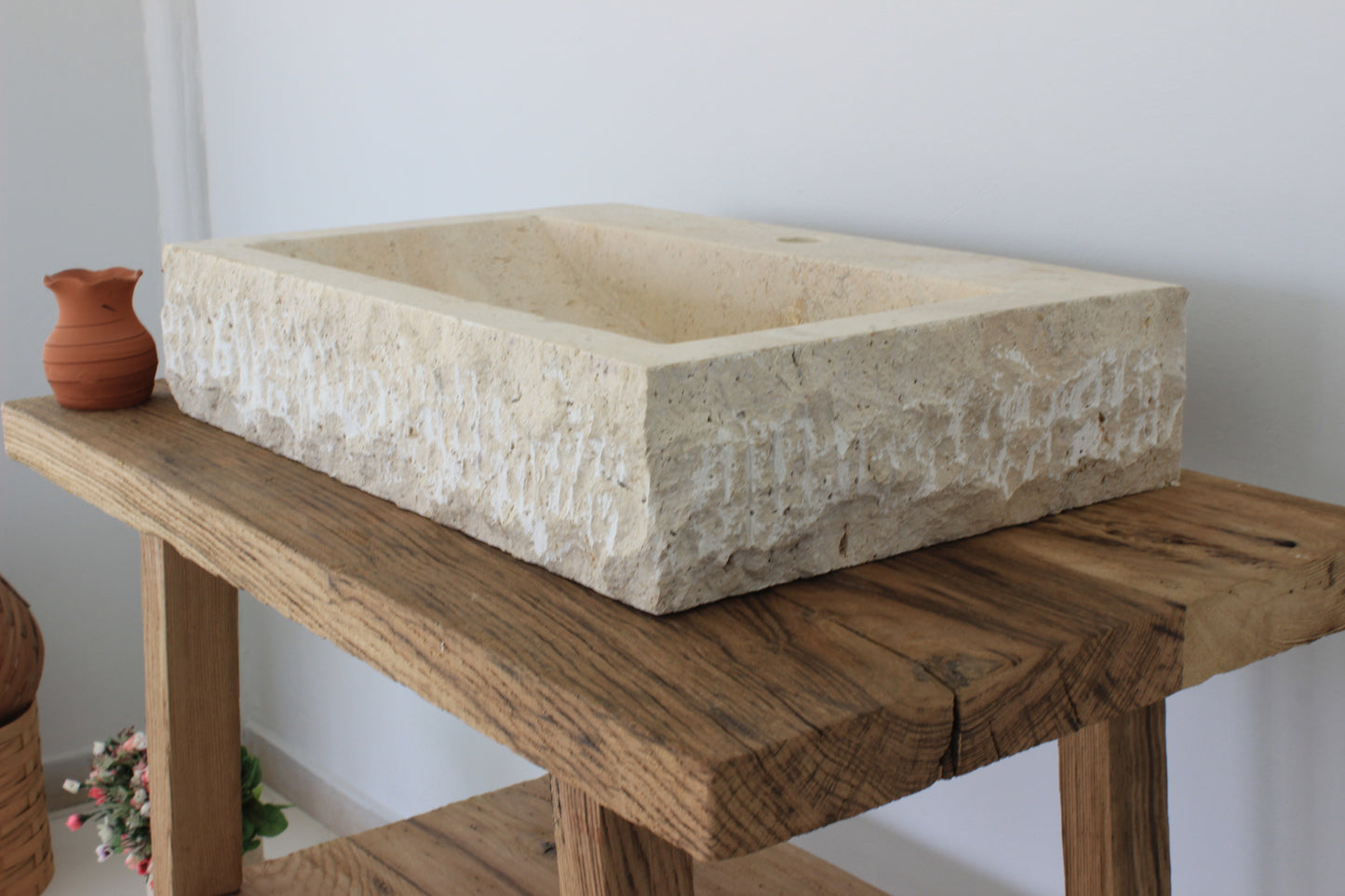 A large Norhew rectangular vessel sink carved from natural travertine with a rugged chiseled exterior and a smooth, clean-lined interior basin.