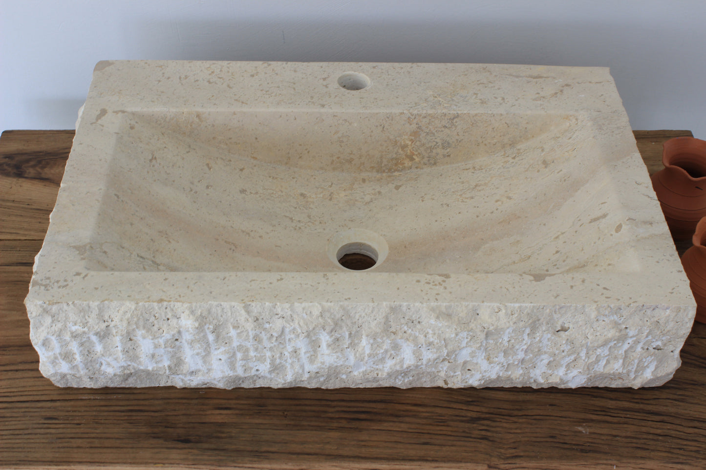A large Norhew rectangular vessel sink carved from natural travertine with a rugged chiseled exterior and a smooth, clean-lined interior basin.
