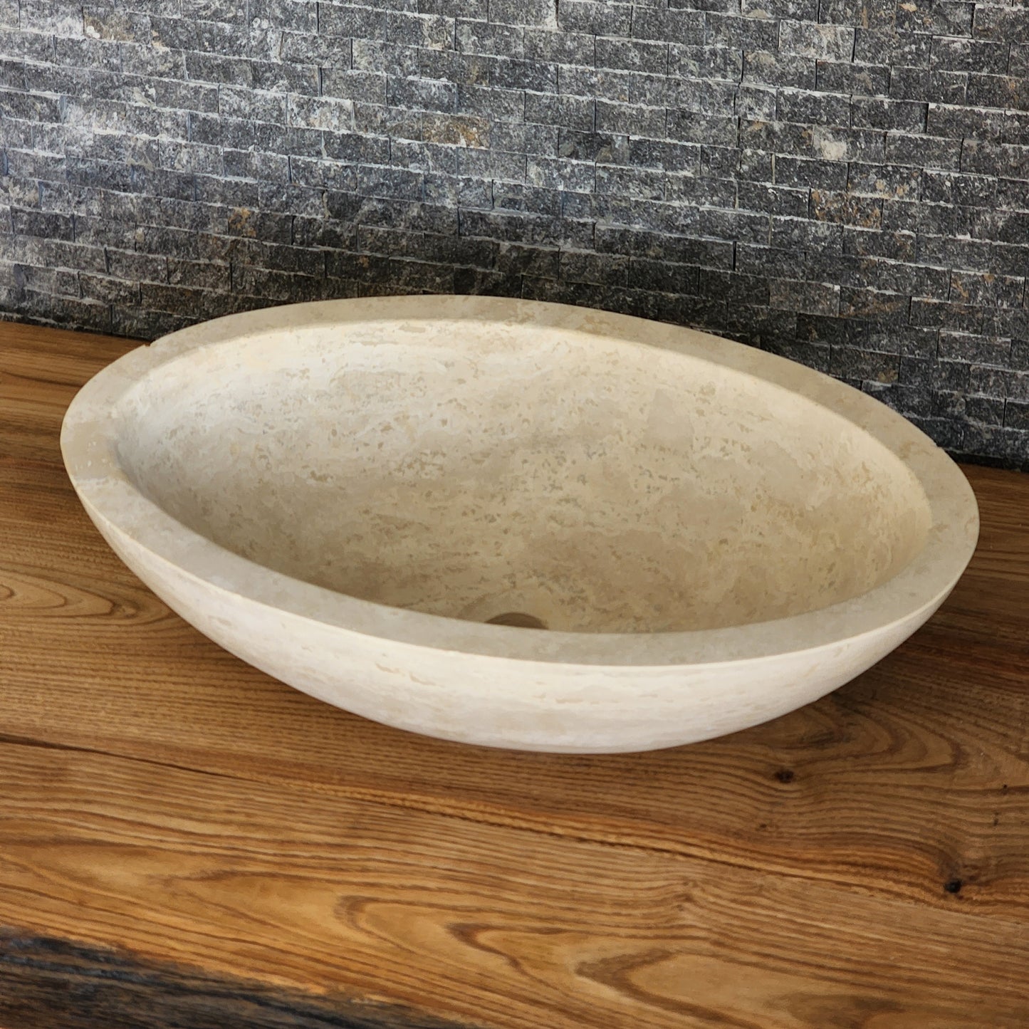 Norhew luxury round solid travertine vessel sink with natural golden-beige pitting and a thick-rimmed profile on a wooden vanity.