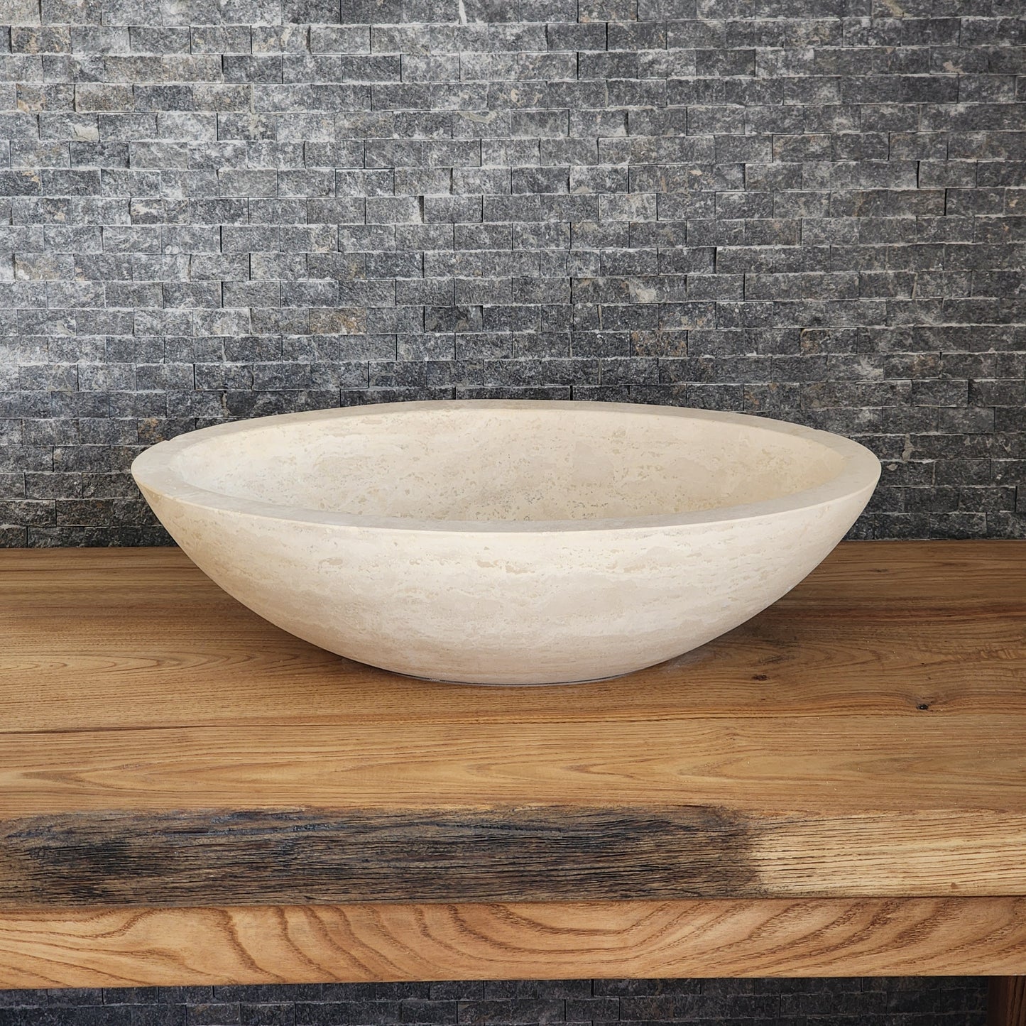 Norhew luxury round solid travertine vessel sink with natural golden-beige pitting and a thick-rimmed profile on a wooden vanity.
