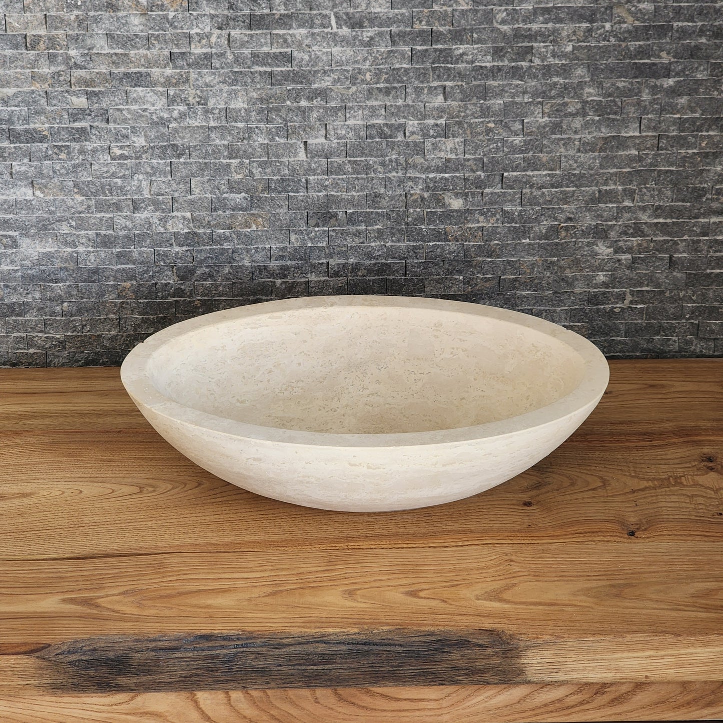 Norhew luxury round solid travertine vessel sink with natural golden-beige pitting and a thick-rimmed profile on a wooden vanity.