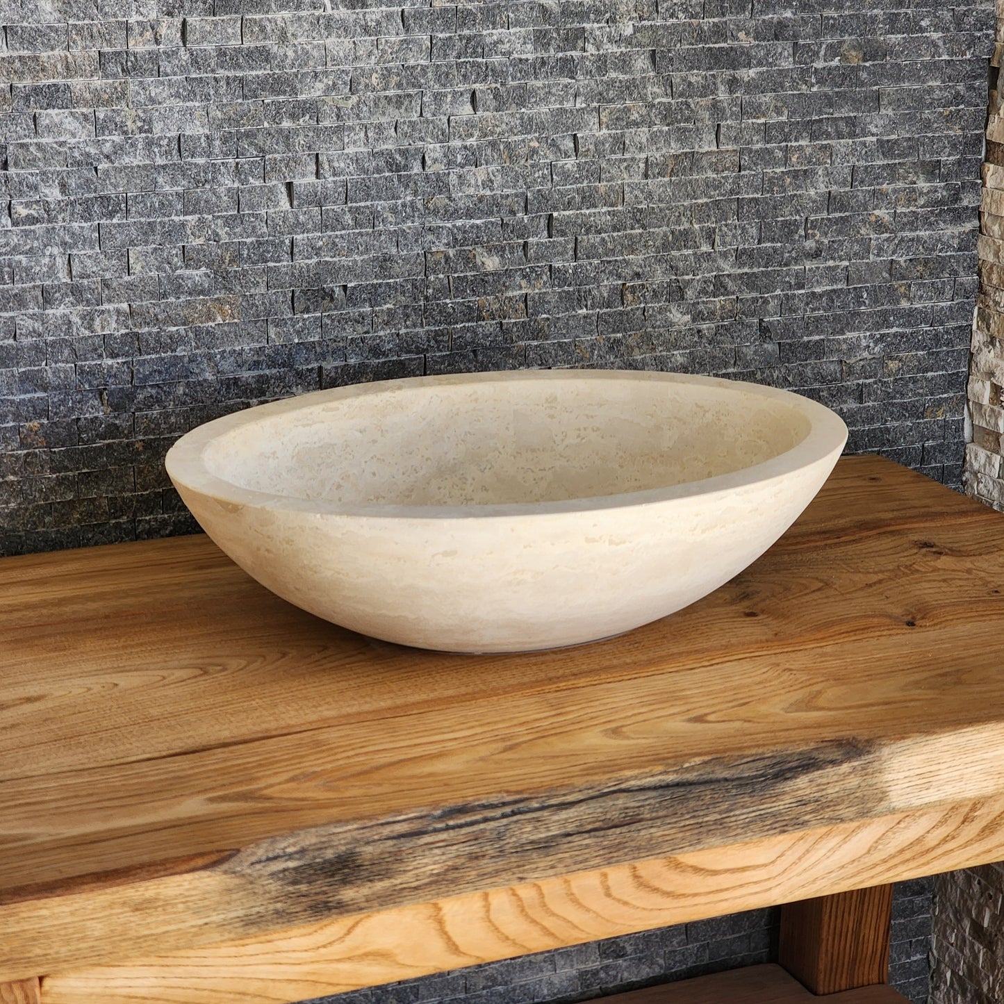Norhew luxury round solid travertine vessel sink with natural golden-beige pitting and a thick-rimmed profile on a wooden vanity.