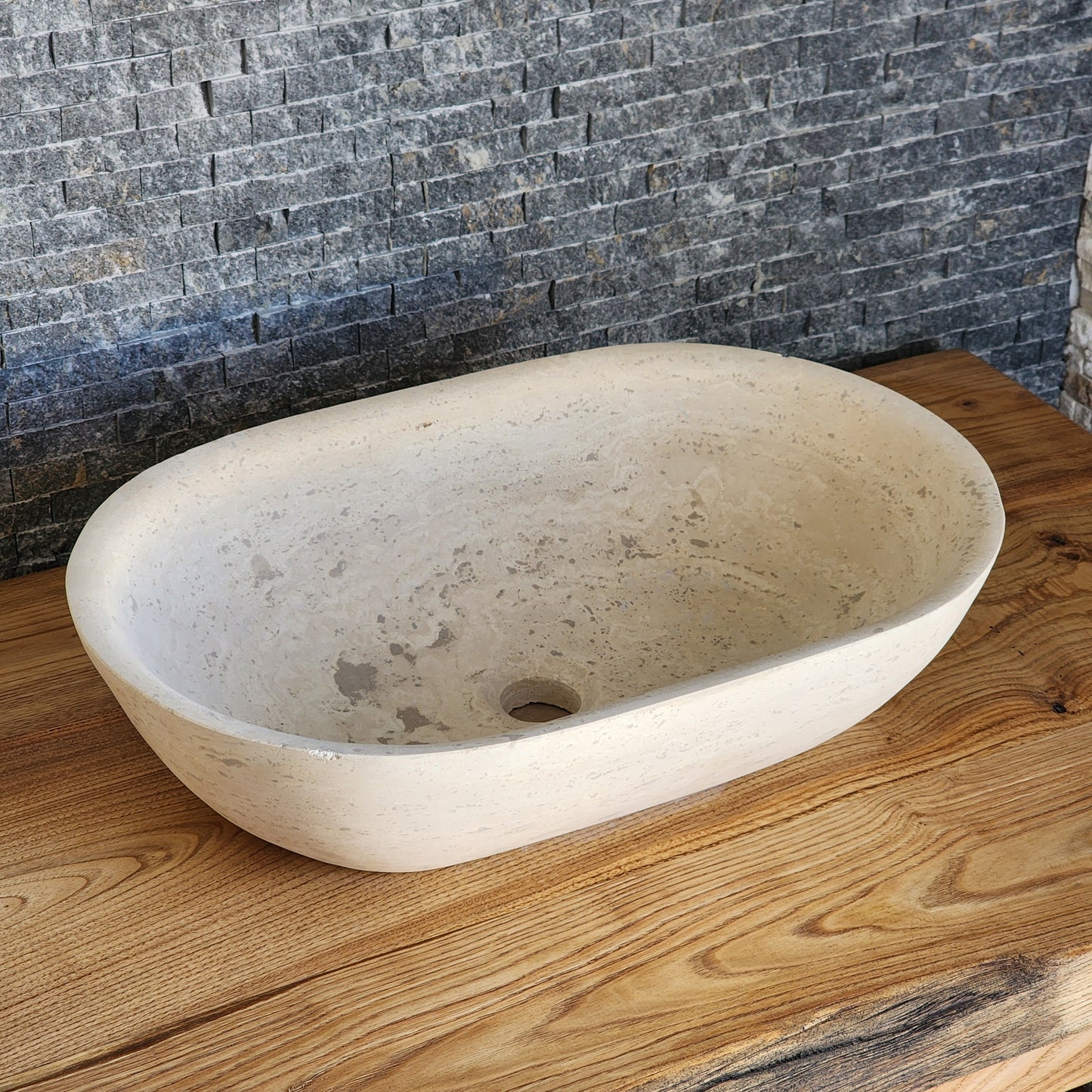 Norhew luxury travertine oval vessel sink with natural cream pitting and a honed finish on a solid wood vanity.